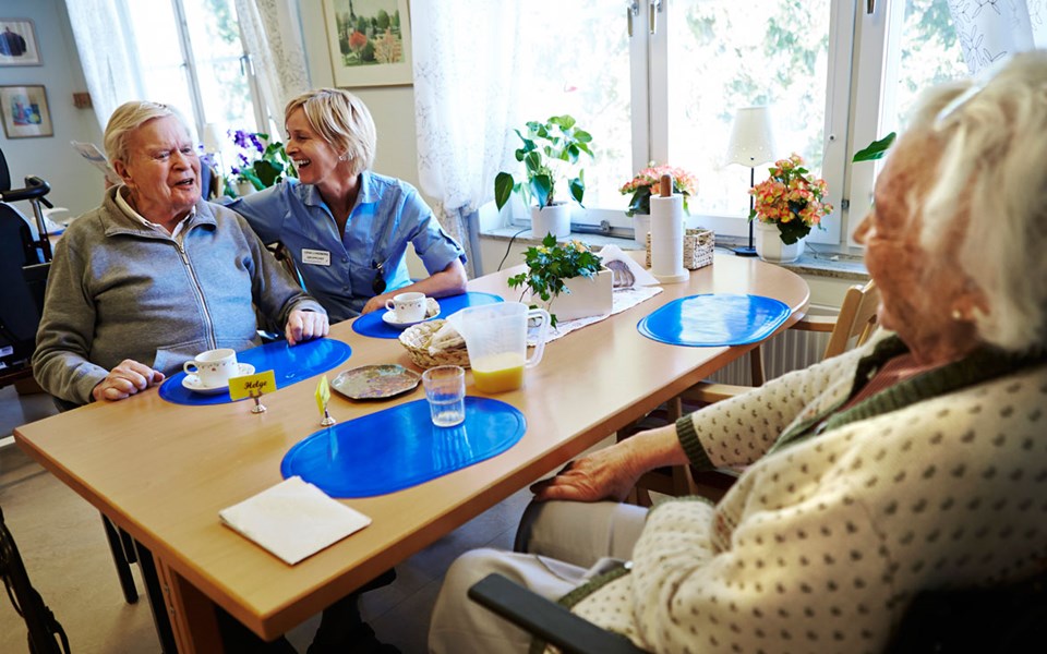 Några äldre personer sitter runt ett bord tillsammans med personal och pratar.
